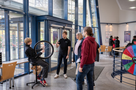 BesucherInnen in einem Foyer probieren Mechanikexperimente mit einem Rad aus.